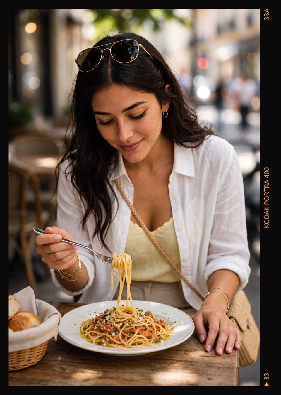 Kaethia_ smiles with her eyes lowered as she lifts a forkful of spaghetti from a plate on a wooden table, sunglasses resting on her dark hair, in soft dappled light.